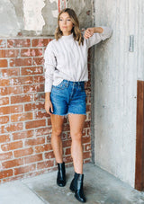 [Color: Light Taupe] A gorgeous cable knit pullover featuring whimsical pom pom details, a warm mock neck, and a contrast ribbed trim.