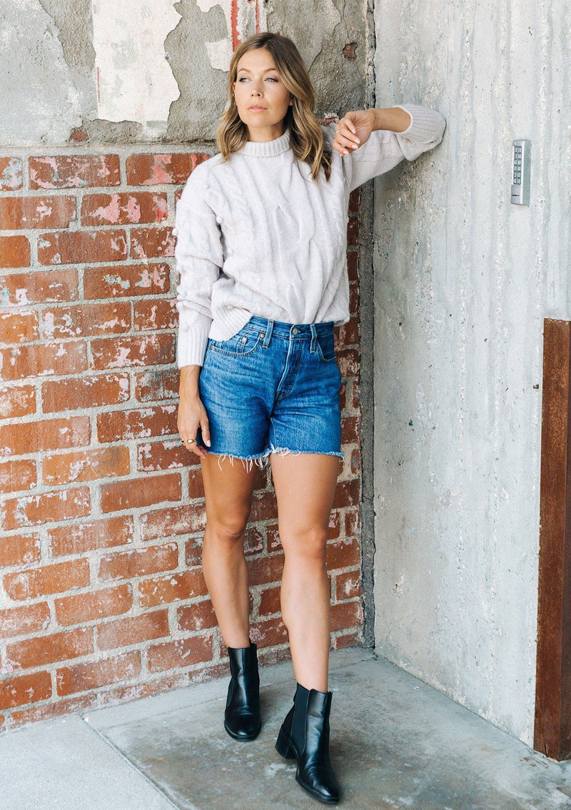 [Color: Light Taupe] A gorgeous cable knit pullover featuring whimsical pom pom details, a warm mock neck, and a contrast ribbed trim.