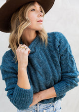 [Color: Teal] A gorgeous cable knit pullover featuring whimsical pom pom details, a warm mock neck, and a contrast ribbed trim.