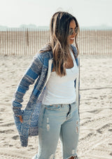 [Color: Denim Blue] Girl at the beach wearing a zipper front striped cardigan.