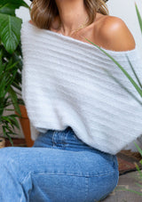 [Color: Grey] A blonde model wearing a fuzzy grey boatneck sweater. The wide neckline can be worn off the shoulder.  