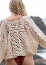 [Color: Natural] A model wearing a natural colored open knit bohemian crochet top with long voluminous sleeves and a wrap front.