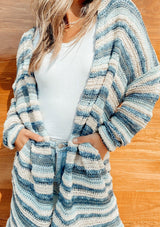 [Color: Blue Natural] A retro striped mid length cardigan. Featuring essential side pockets and subtle metallic details throughout that catch the light. Paired here with jeans and boots.