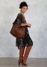 [Color: Brown] A brown leather bag with patchwork stitch exterior, double leather straps, and o ring detail. 