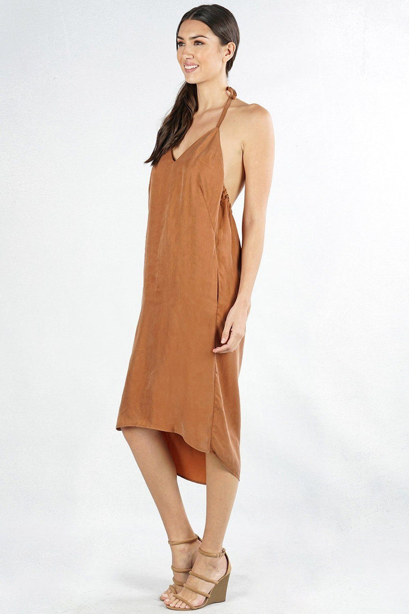 [Color: Bronze] A side facing image of a brunette model wearing an olive green high-low halter dress featuring a v-neckline, open back, side pockets, and an adjustable drawstring tie at the back for a chic finish.