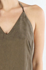 [Color: Olive] A detail image of a brunette model wearing an olive green high-low halter dress featuring a v-neckline, open back, side pockets, and an adjustable drawstring tie at the back for a chic finish.