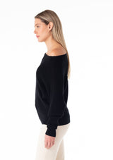 [Color: Black] A side facing image of a blonde model wearing a black waffle knit pullover sweater. With long sleeves, a relaxed fit, and a wide neckline that can be worn off the shoulder.
