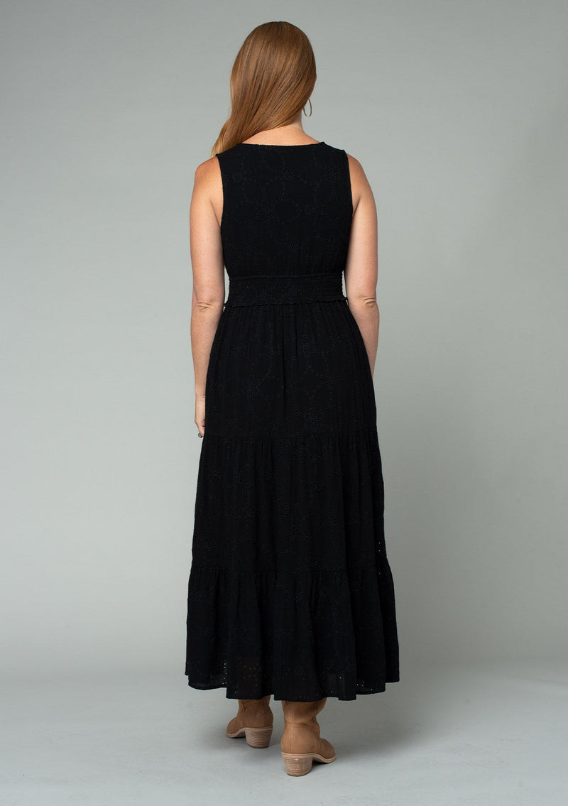 [Color: Black] A back facing image of a red headed model wearing a sleeveless black bohemian eyelet maxi dress. With a v neckline, a long tiered skirt, and a smocked elastic waist. A classic bohemian black maxi dress for Summer.
