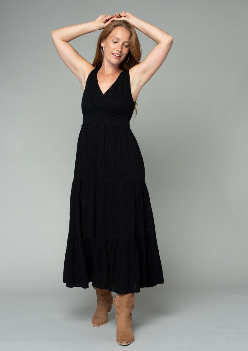 [Color: Black] A front facing image of a red headed model wearing a sleeveless black bohemian eyelet maxi dress. With a v neckline, a long tiered skirt, and a smocked elastic waist. A classic bohemian black maxi dress for Summer.