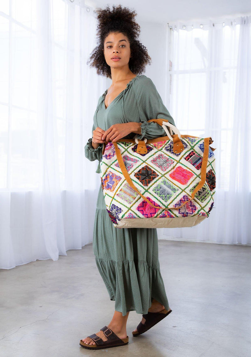 [Color: Multi/Natural] A model holding a patchwork weekender bag. With embroidered details, suede trim, suede top handles, and a suede long adjustable strap.