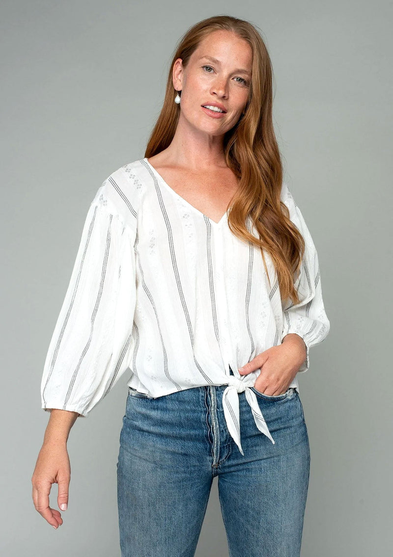[Color: Off White/Black] A front facing image of a red headed model wearing a white long sleeve bohemian top with a thin black yarn dye stripe throughout. With a v neckline and a tie waist detail. 