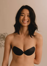 [Color: Noir] A model wearing a black gatherall silicone  strapless bra. 