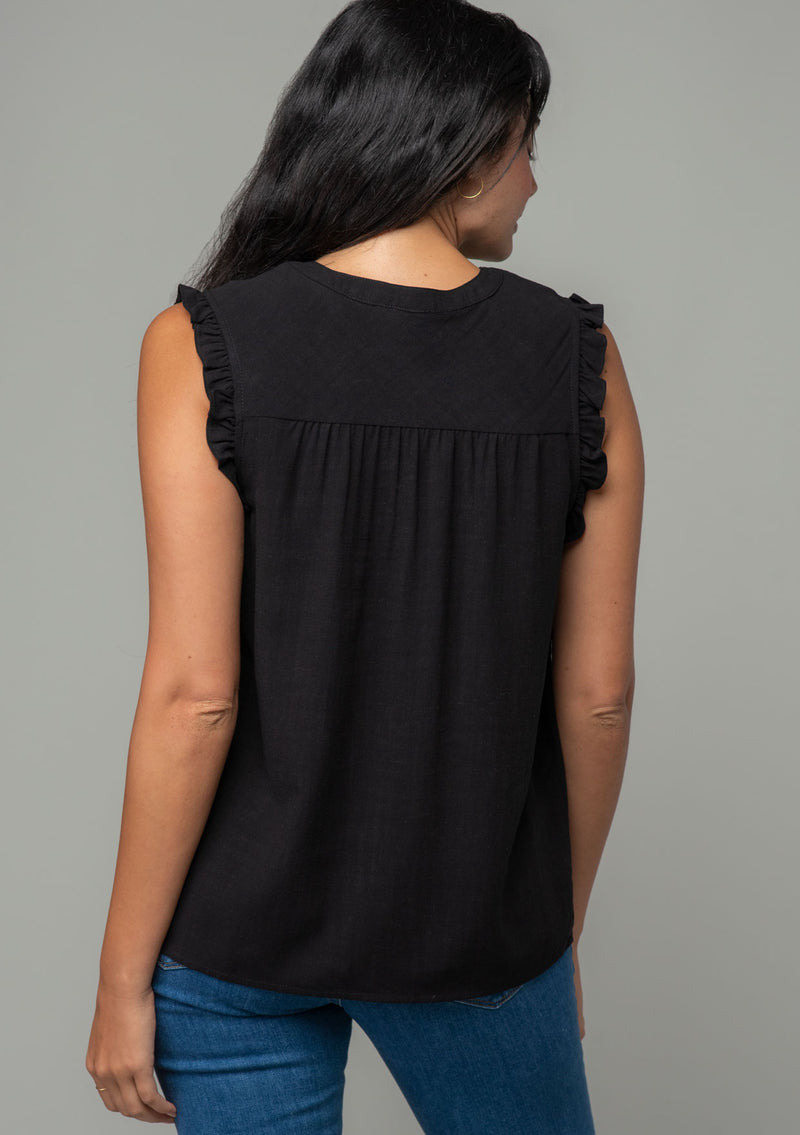 [Color: Black] A back facing image of a brunette model wearing a black linen blend bohemian top with short ruffled cap sleeves, a v neckline, and a flowy silhouette.
