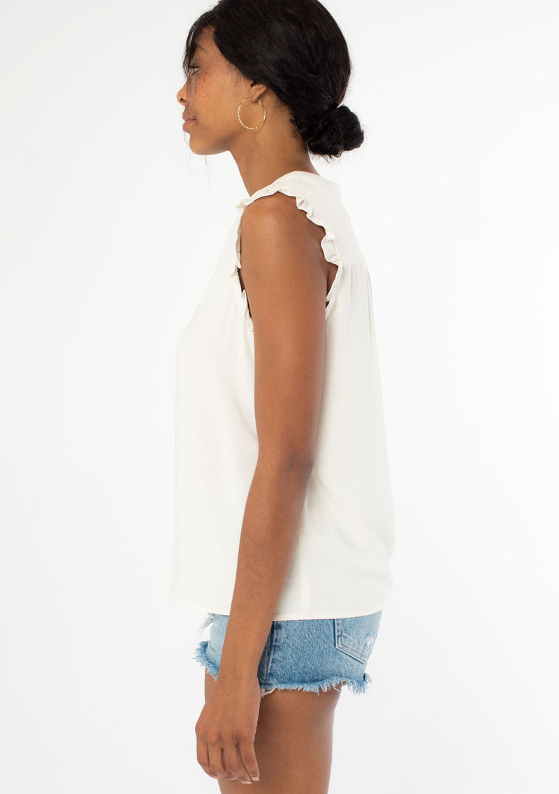 [Color: Natural] A side facing image of a black model wearing a natural, off white linen blend bohemian top with short ruffled cap sleeves, a v neckline, and a flowy silhouette. 