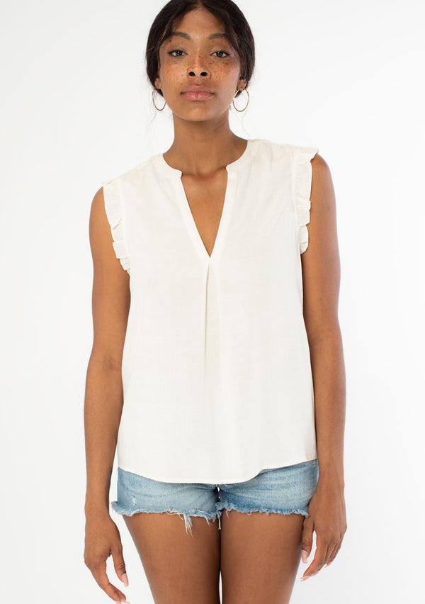 [Color: Natural] A front facing image of a black model wearing a natural, off white linen blend bohemian top with short ruffled cap sleeves, a v neckline, and a flowy silhouette. 