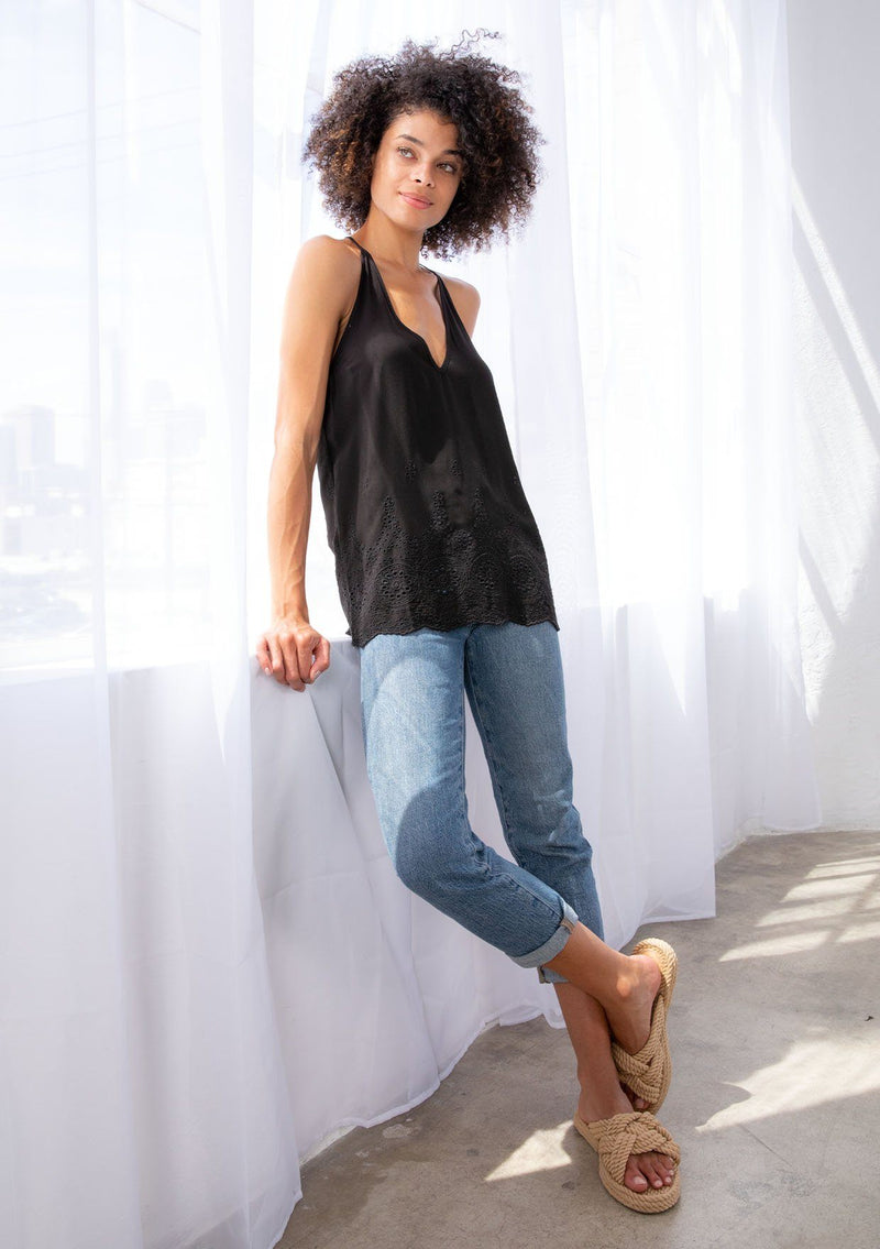 [Color: Black] A model wearing a lightweight tank top with embroidered eyelet detail. With a scalloped hemline, a racer back, and a v neckline.