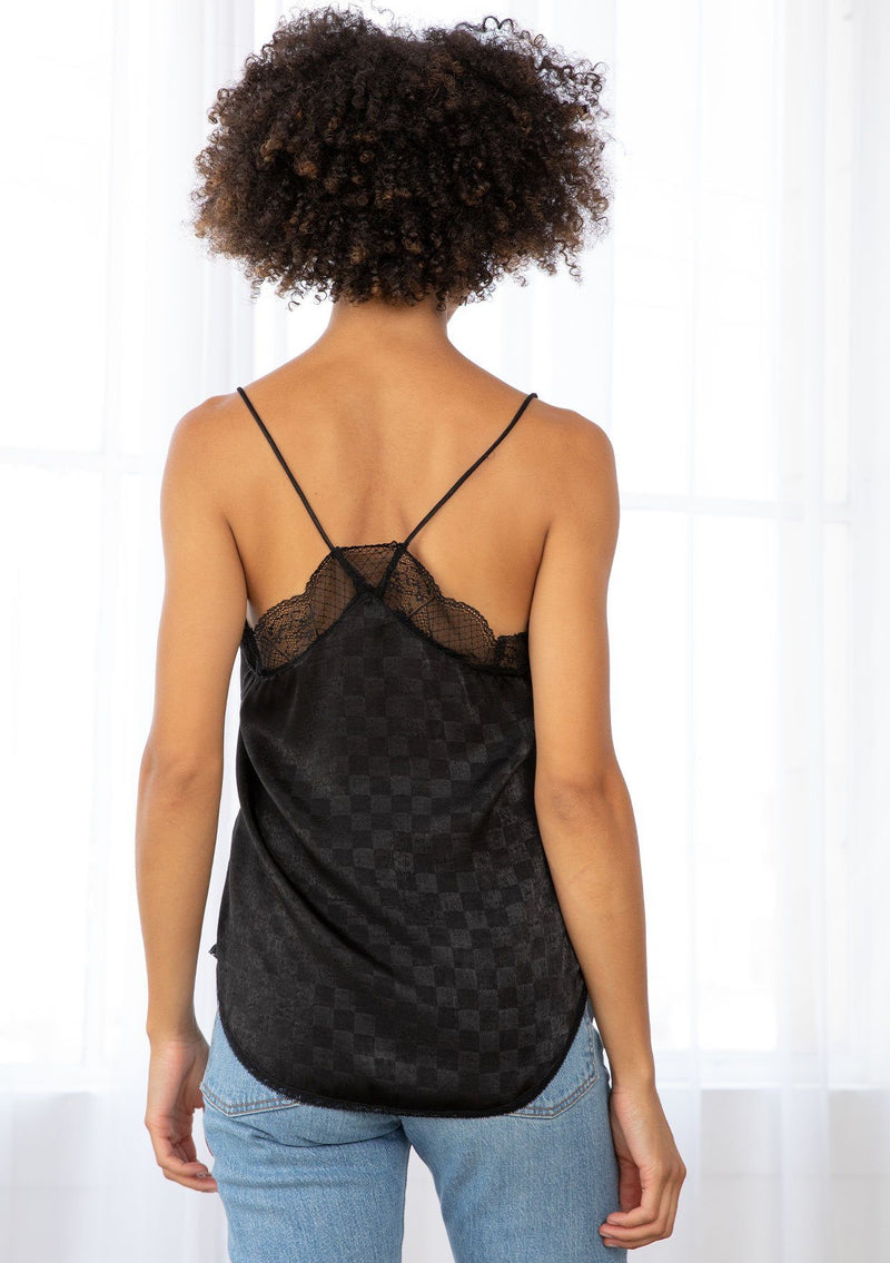 [Color: Black] A model wearing a black checkered jacquard silky slip camisole. With adjustable spaghetti straps and a lace trim v neckline and racerback. 