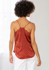 [Color: Burnt Rust] A model wearing a rust red checkered jacquard silky slip camisole. With adjustable spaghetti straps and a lace trim v neckline and racerback. 