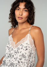 [Color: Natural/Black] A close up front facing image of a brunette model wearing a natural off white and black floral print camisole. With a lace trim v neckline and racer back and adjustable spaghetti straps. 