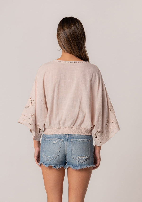 [Color: Natural] A back facing image of a brunette model wearing a bohemian natural light brown embroidered eyelet top with billowy half length sleeves, a button front, and a v neckline.
