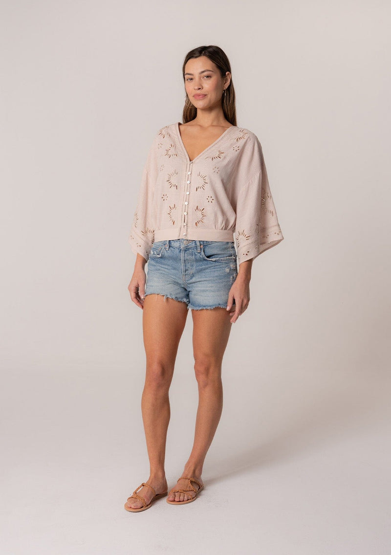 [Color: Natural] A full body front facing image of a brunette model wearing a bohemian natural light brown embroidered eyelet top with billowy half length sleeves, a button front, and a v neckline.