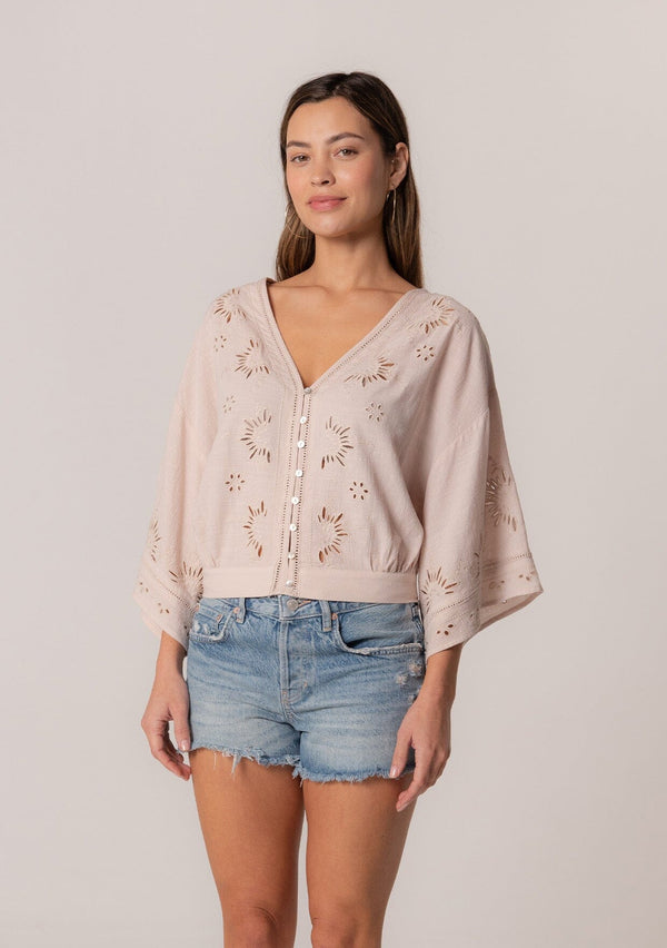 [Color: Natural] A front facing image of a brunette model wearing a bohemian natural light brown embroidered eyelet top with billowy half length sleeves, a button front, and a v neckline.