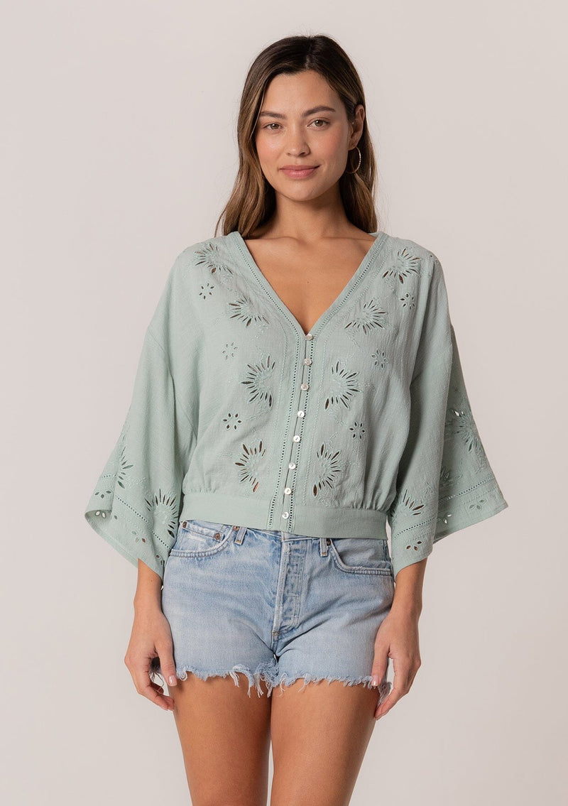 [Color: Seafoam] A front facing image of a brunette model wearing a bohemian seafoam green embroidered eyelet top with billowy half length sleeves, a button front, and a v neckline.