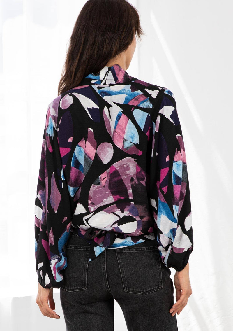 [Color: Black/Plum] A model wearing a black and purple watercolor print kimono wrap top. With long voluminous sleeves, an elastic wrist cuff, and a built in tie front that can be tied in multiple ways. 
