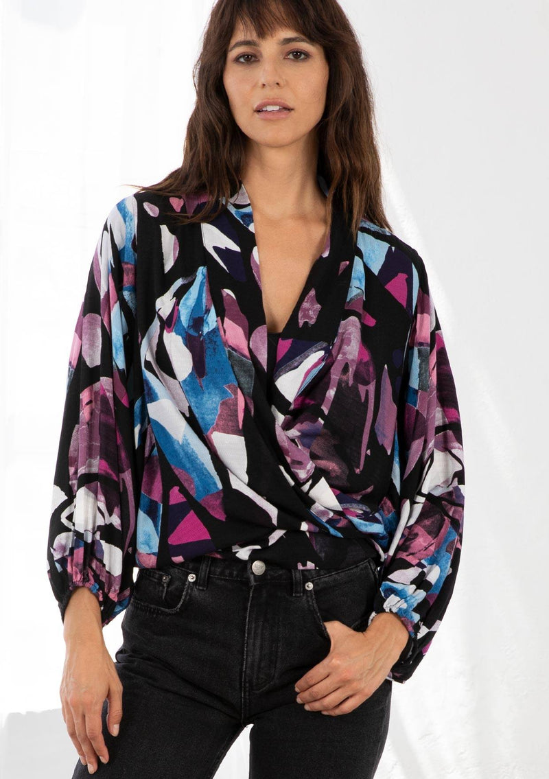 [Color: Black/Plum] A model wearing a black and purple watercolor print kimono wrap top. With long voluminous sleeves, an elastic wrist cuff, and a built in tie front that can be tied in multiple ways. 