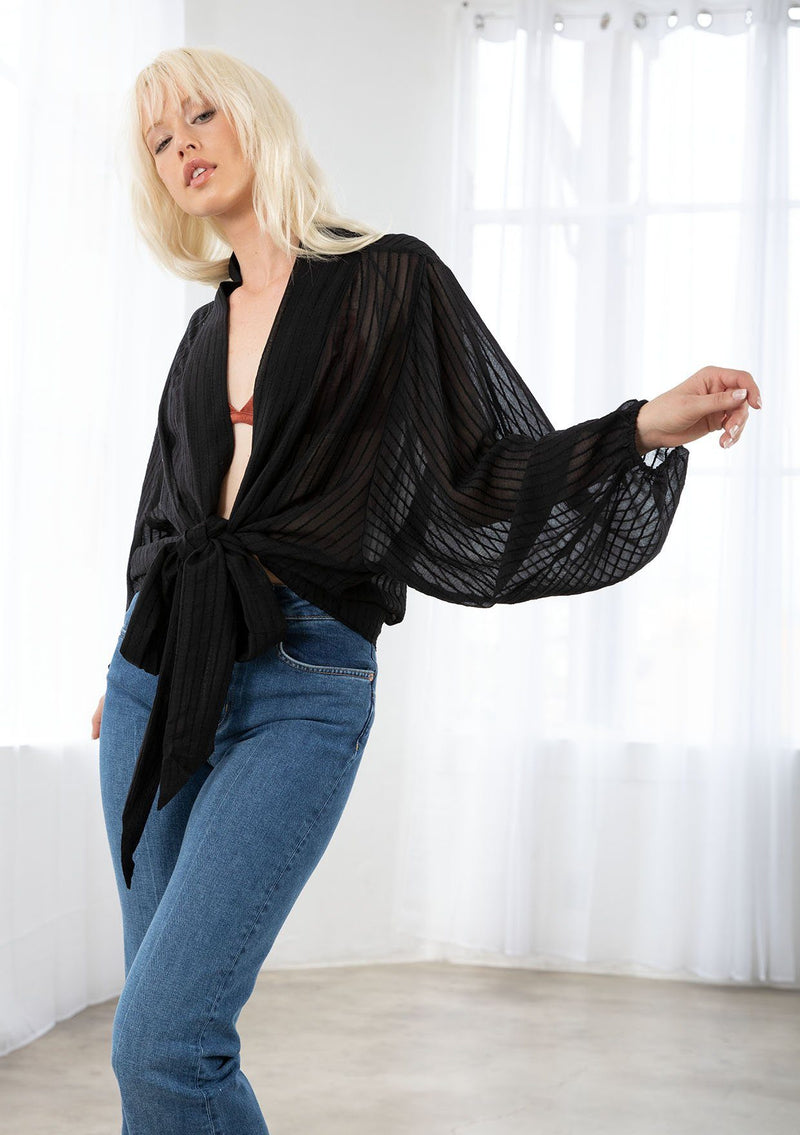 [Color: Black] A model wearing a soft sheer black kimono top in a tonal shadow stripe. With long voluminous sleeves, elastic wrist cuffs, and a wrap tie front that can be tied in multiple ways. 