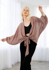 [Color: Dusty Rose] A model wearing a soft sheer dusty rose kimono top in a tonal shadow stripe. With long voluminous sleeves, elastic wrist cuffs, and a wrap tie front that can be tied in multiple ways. 