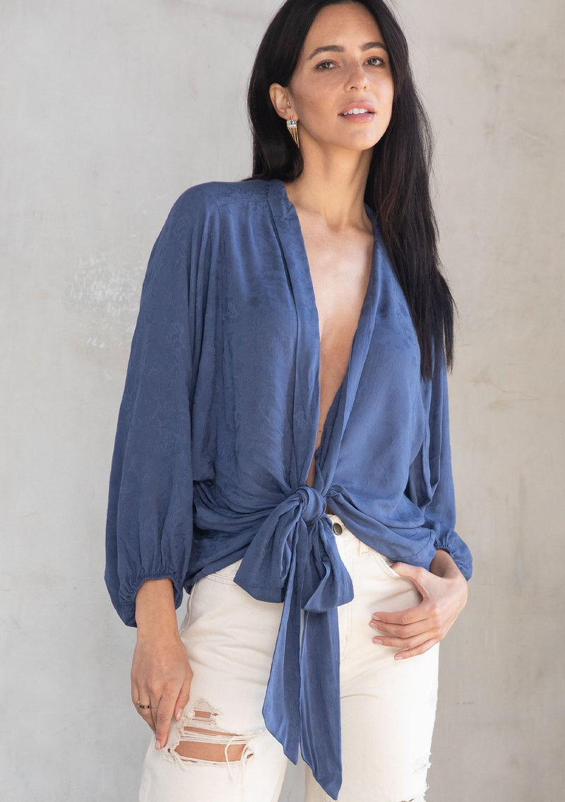 [Color: Indigo Blue] A model wearing an elegant blue bohemian kimono top in textured floral jacquard. Features dolman sleeves, a deep v neckline and tie front. Can be tied in multiple ways.