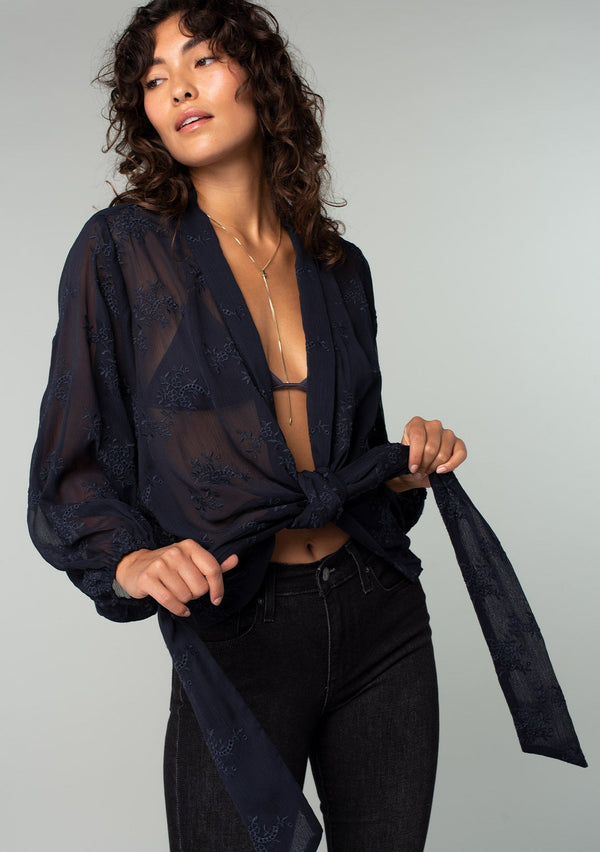 [Color: Navy] A front facing image of a brunette model wearing a navy blue bohemian embroidered chiffon kimono top. With long sleeves and a tie front that can be styled in multiple ways. 