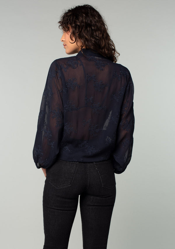 [Color: Navy] A back facing image of a brunette model wearing a navy blue bohemian embroidered chiffon kimono top. With long sleeves and a tie front that can be styled in multiple ways. 