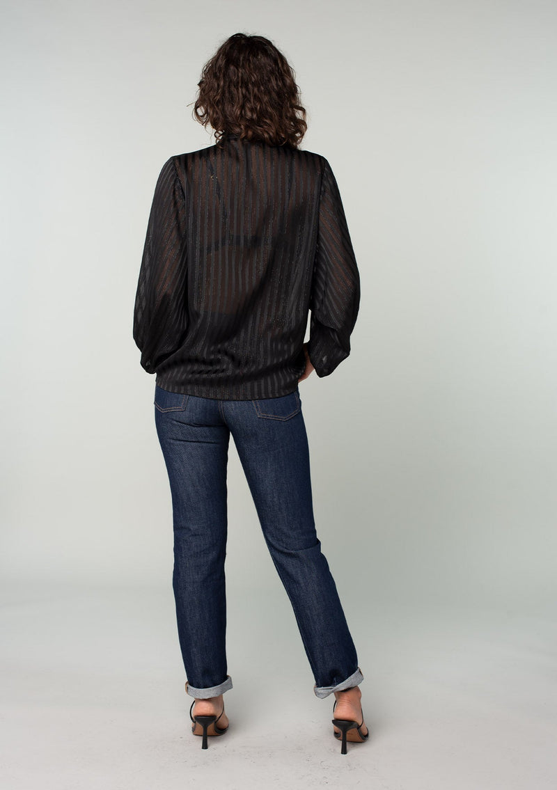 [Color: Black] A back facing image of a brunette model wearing a sheer black bohemian tie front top in a sparkly lurex stripe. With voluminous long sleeves and a tie front waist that can be styled in multiple ways. 
