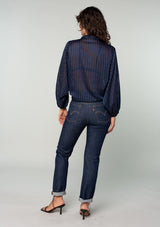 [Color: Navy] A back facing image of a brunette model wearing a sheer navy blue bohemian tie front top in a sparkly lurex stripe. With voluminous long sleeves and a tie front waist that can be styled in multiple ways. 