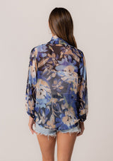 [Color: Navy/Light Blue] A back facing image of a brunette model wearing a sheer chiffon tie front top in a blue floral print. With long sleeves, a deep v neckline, a flowy relaxed fit, and a tie front waist detail. 