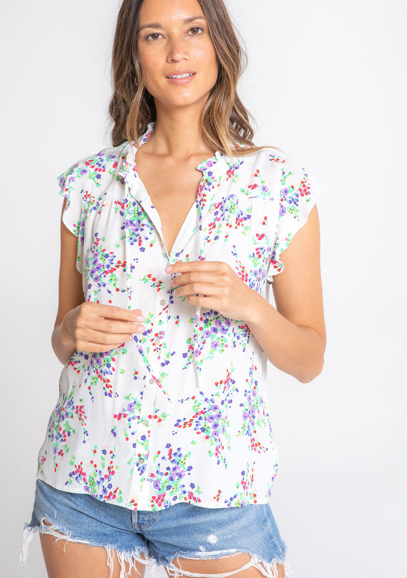 [Color: Ivory/Violet] A model wearing a bohemian white short flutter sleeve button front top in a purple floral print. 