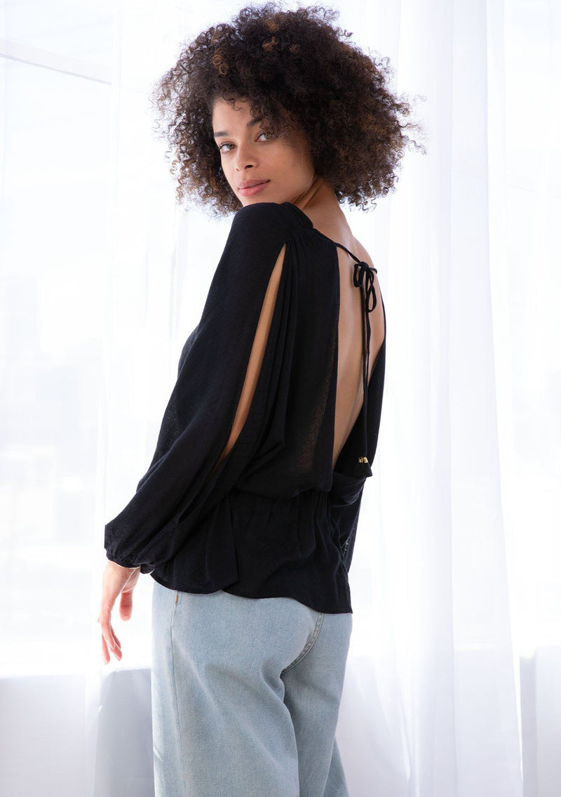 [Color: Black] A model wearing a lightweight black blouse. With long voluminous split sleeves, an open back with tassel tie closure, and an adjustable drawstring waist. 