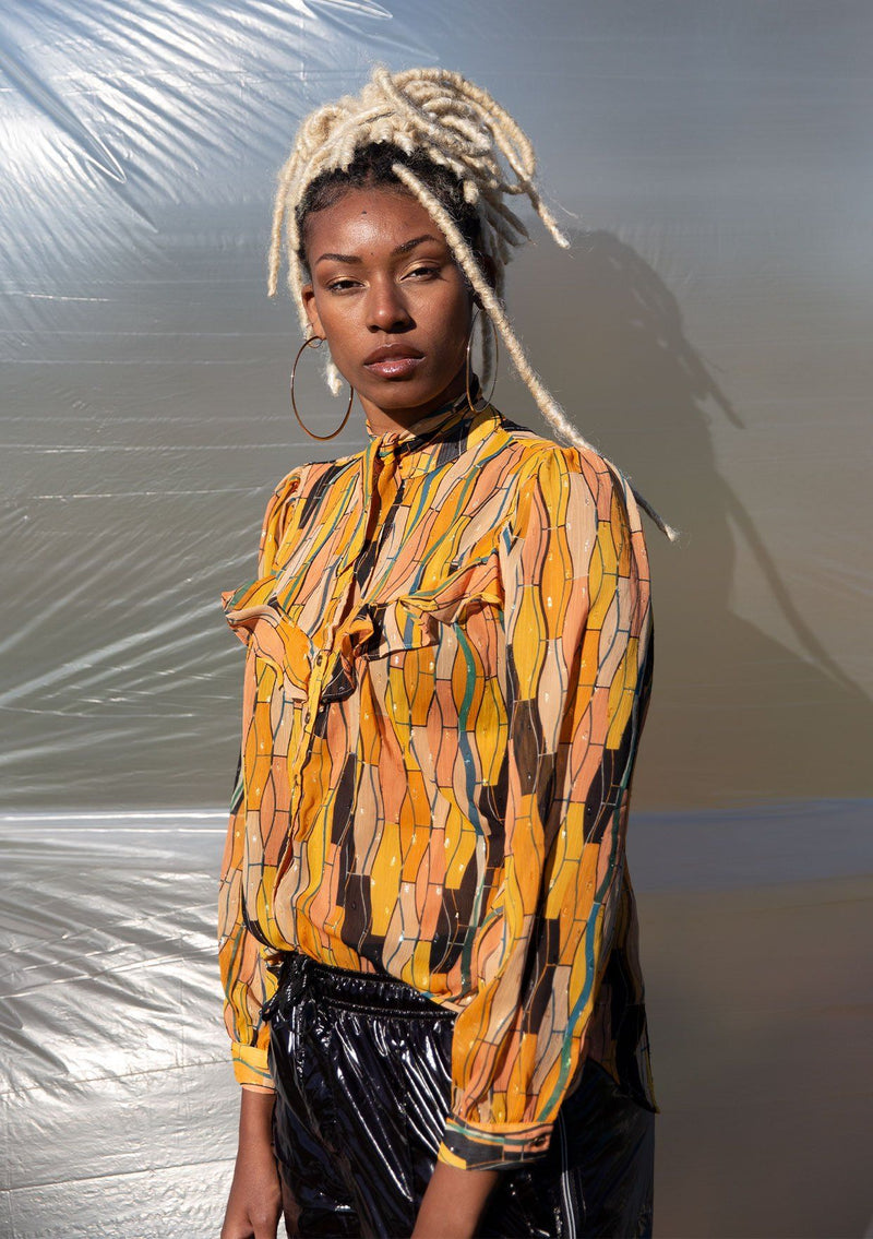 [Color: Honey Gold] A button up blouse in a vintage inspired tile print. Featuring a flirty ruffle yoke detail and a split neckline with ties. A subtle metallic detail throughout adds a little sparkle to this bohemian top. 