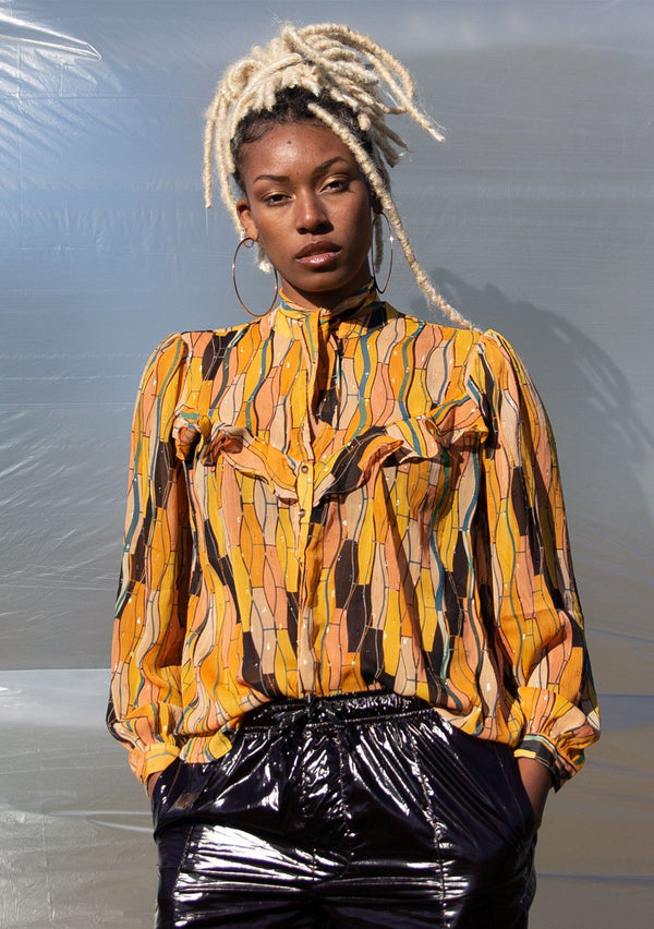 [Color: Honey Gold] A button up blouse in a vintage inspired tile print. Featuring a flirty ruffle yoke detail and a split neckline with ties. A subtle metallic detail throughout adds a little sparkle to this bohemian top. 