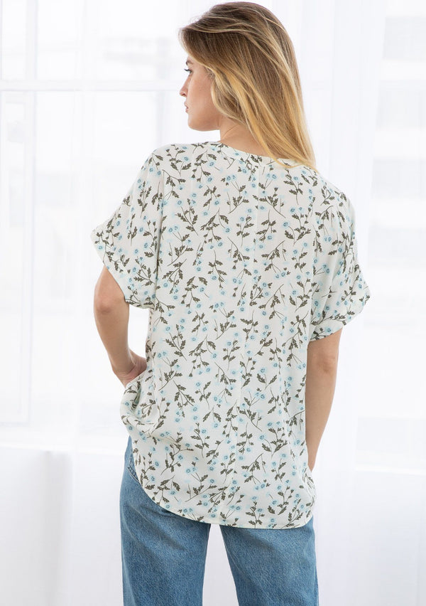 [Color: Ivory/Sky] A blond model wearing a short sleeve top in a floral print. With a cuffed dolman sleeve, a split v neckline, and an easy popover style silhouette. 
