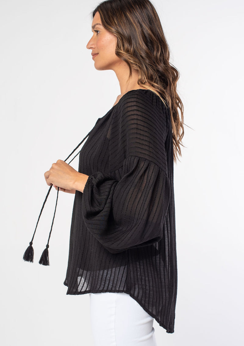 [Color: Black] A woman wearing a black textured shadow striped flowy bohemian peasant top with voluminous long sleeves and a split neckline with tassel ties.