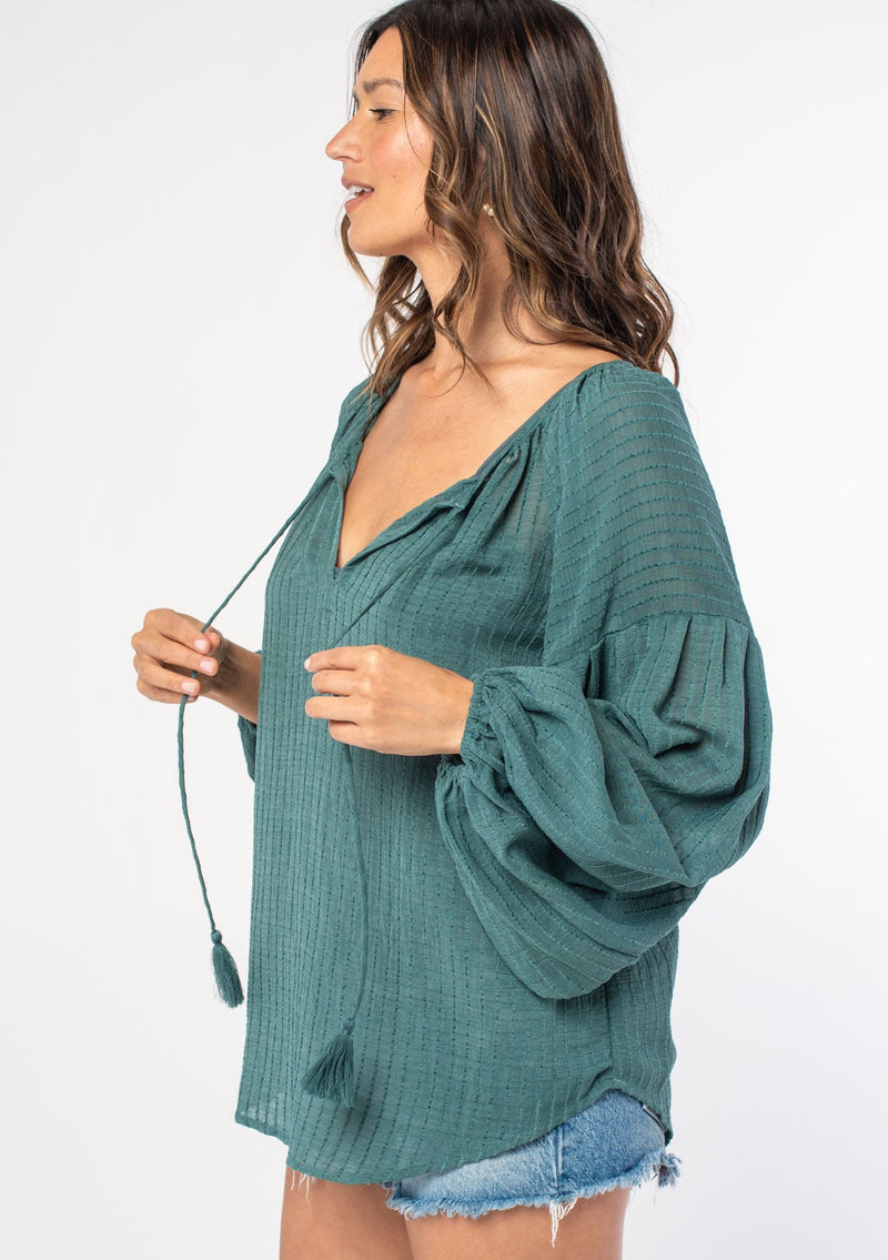 [Color: Sea Green] A woman wearing a green textured shadow striped flowy bohemian peasant top with voluminous long sleeves and a split neckline with tassel ties.