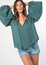 [Color: Sea Green] A woman wearing a green textured shadow striped flowy bohemian peasant top with voluminous long sleeves and a split neckline with tassel ties.