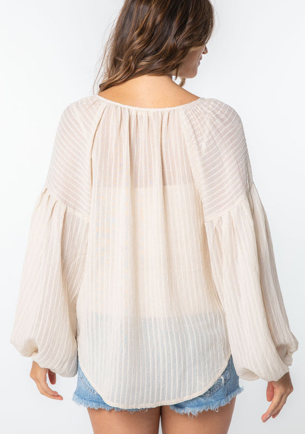 [Color: Vanilla] A woman wearing an off white textured shadow striped flowy bohemian peasant top with voluminous long sleeves and a split neckline with tassel ties. 