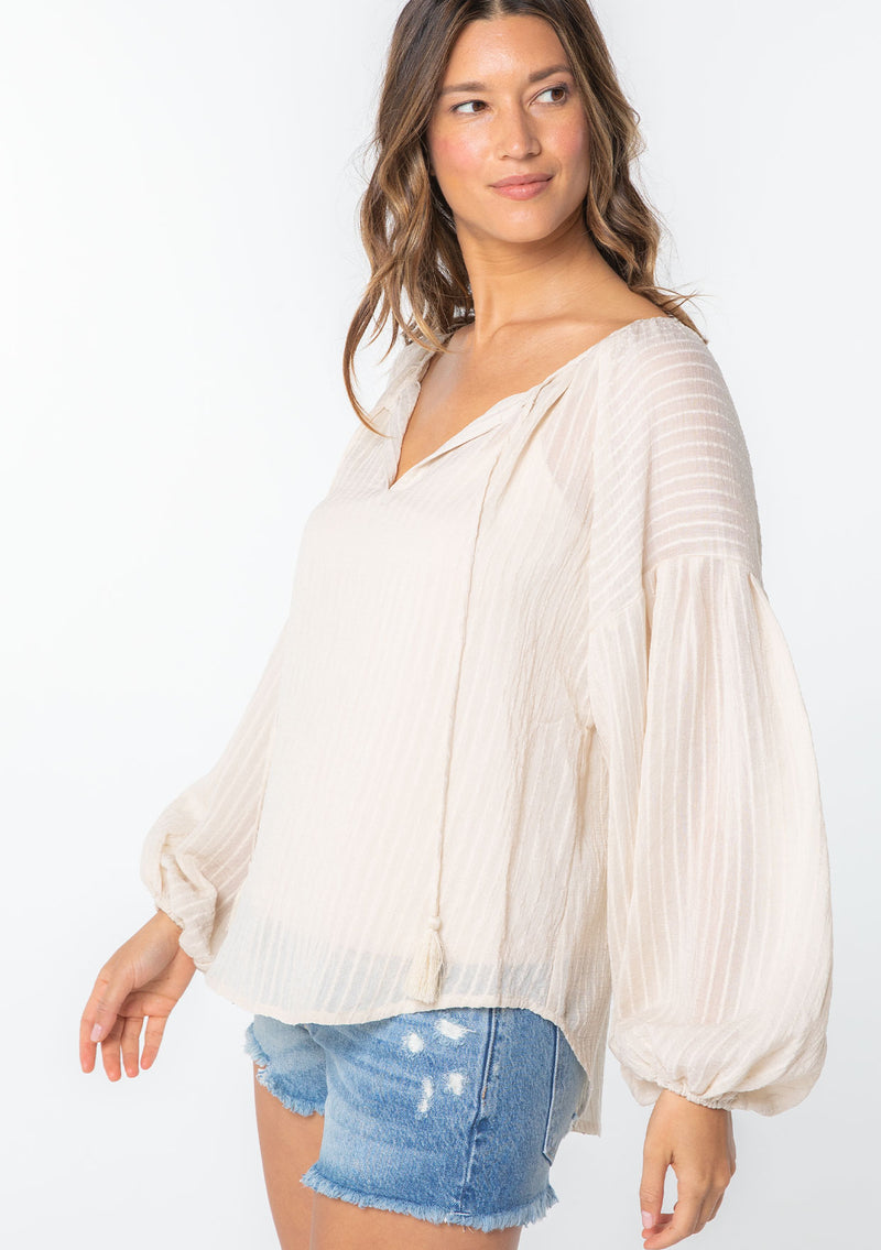 [Color: Vanilla] A woman wearing an off white textured shadow striped flowy bohemian peasant top with voluminous long sleeves and a split neckline with tassel ties. 