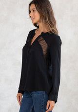 [Color: Black] A model wearing a black blouse with sheer lace inserts. Featuring long sleeves with a button cuff wrist, a self covered button front, and pleated details at the back. 