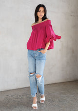 [Color: Mulberry] A model wearing a classic dark pink bohemian blouse in rose jacquard. With three quarter length sleeves, a flounce cuff, and a smocked off shoulder.
