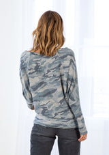 [Color: Olive/Sage] A model wearing an ultra soft Hacci knit pullover in a camouflage print. With long tapered dolman sleeves and a boat neckline that can be worn on or off the shoulder. 